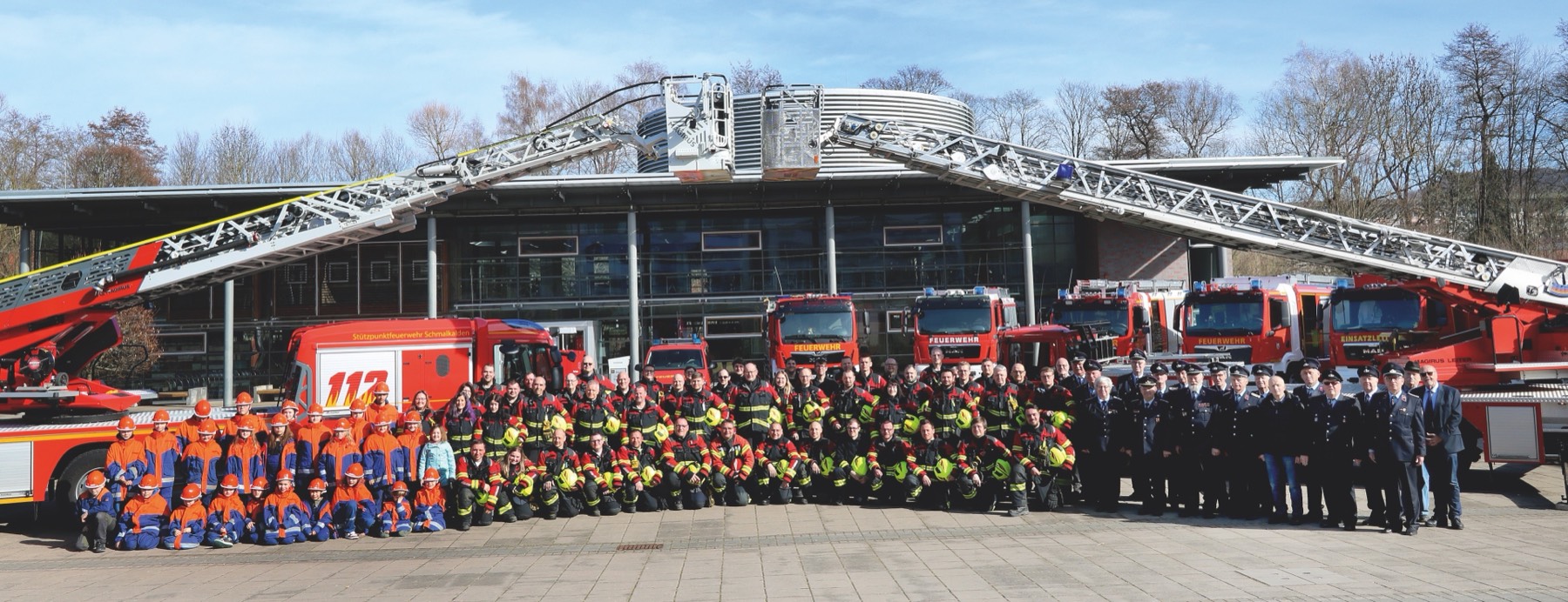 Die gesamte Feuerwehr Schmalkalden mit Fahrzeugen und gekreuzten Drehleitern vor dem Gerätehaus
